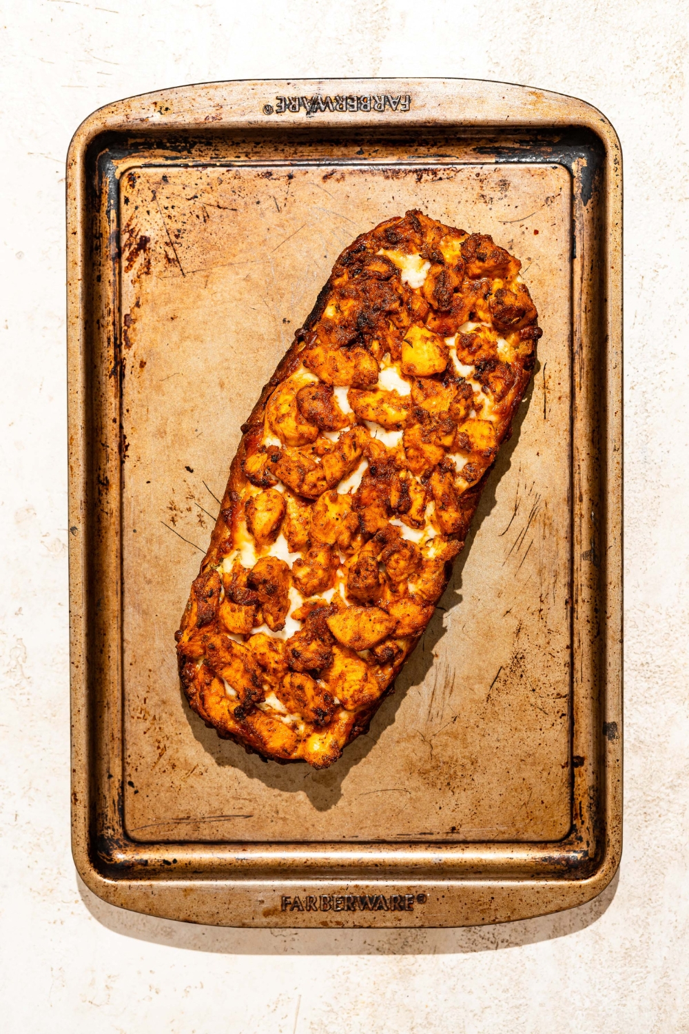 A baking sheet with baked Buffalo chicken garlic bread. The sheet is on a tan counter.