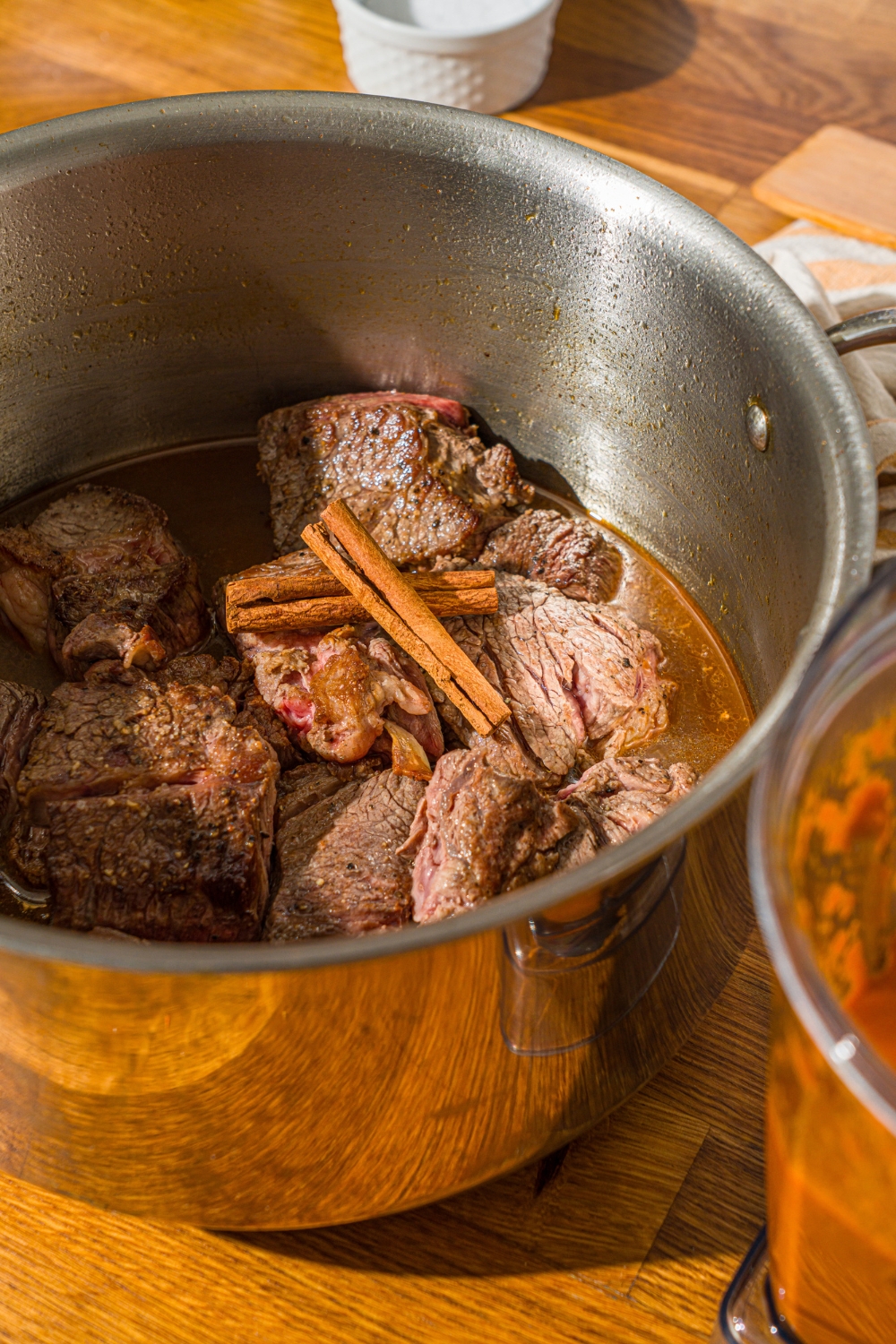 A large stock pot with seared chuck roast with broth and cinnamon sticks.