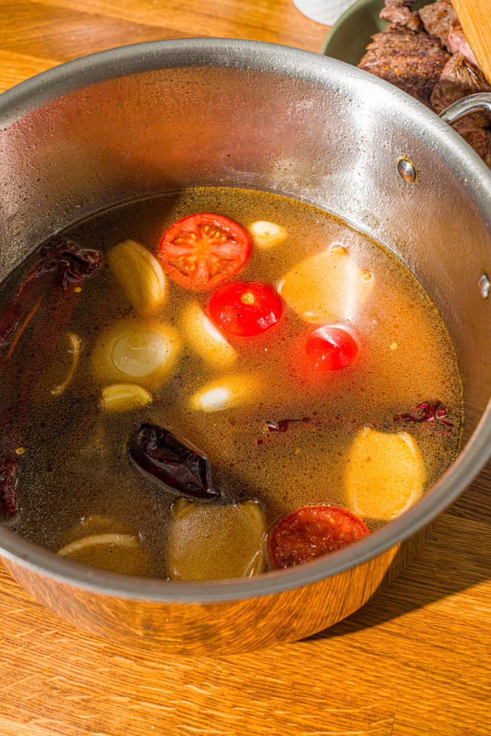 A large stock pot with onions, tomatoes, and peppers cooking in water. The pot is on a wooden counter.