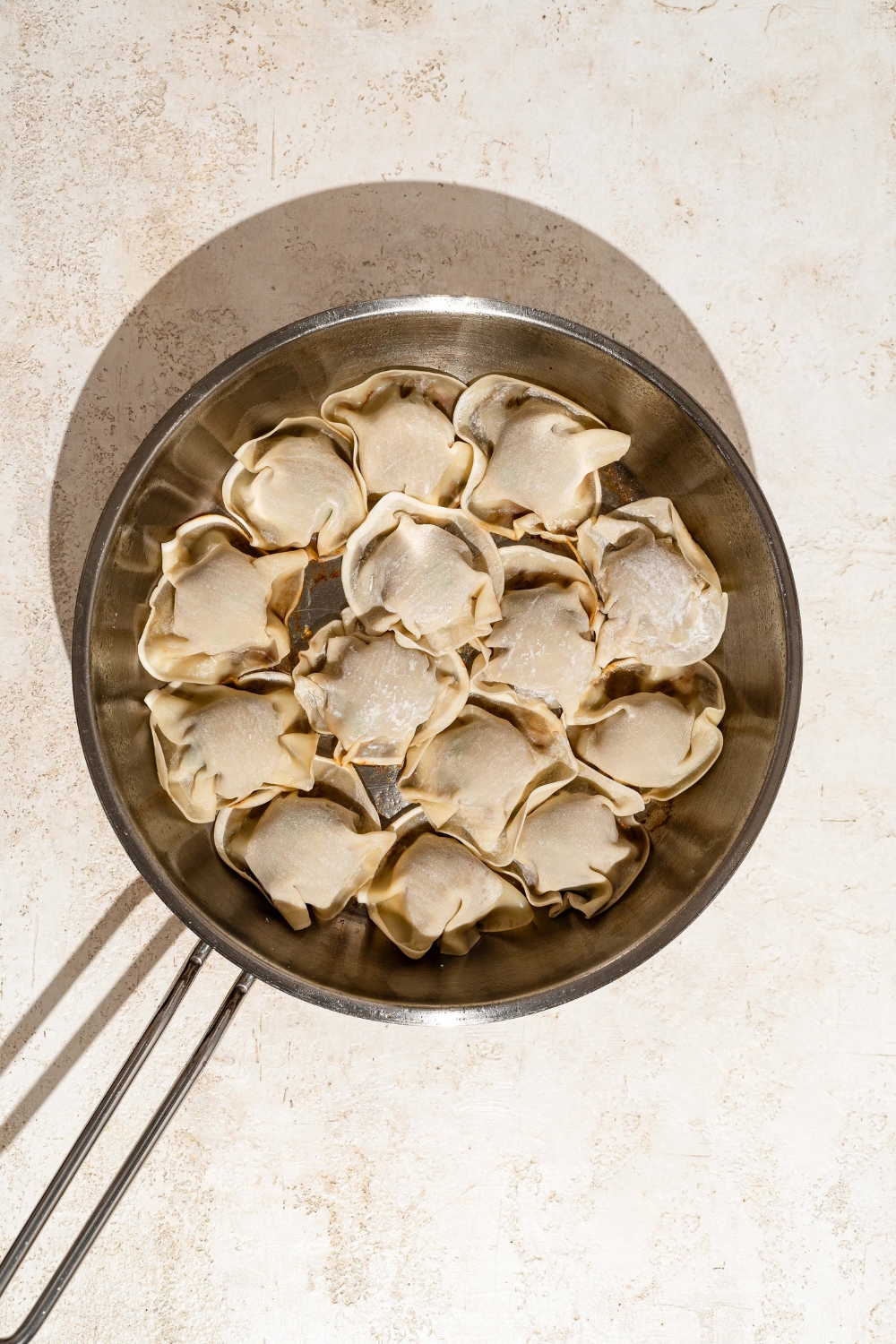 A skillet with balls of ground chicken mixture topped with dumpling wrappers. The skillet is on a tan counter.