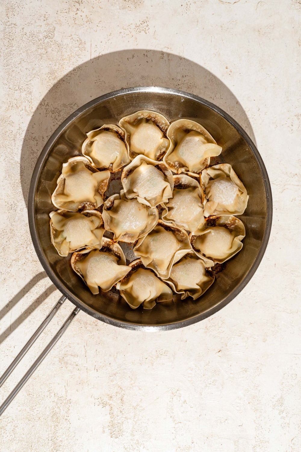 A skillet with blanket dumplings seared on the bottom. The skillet is on a tan counter.