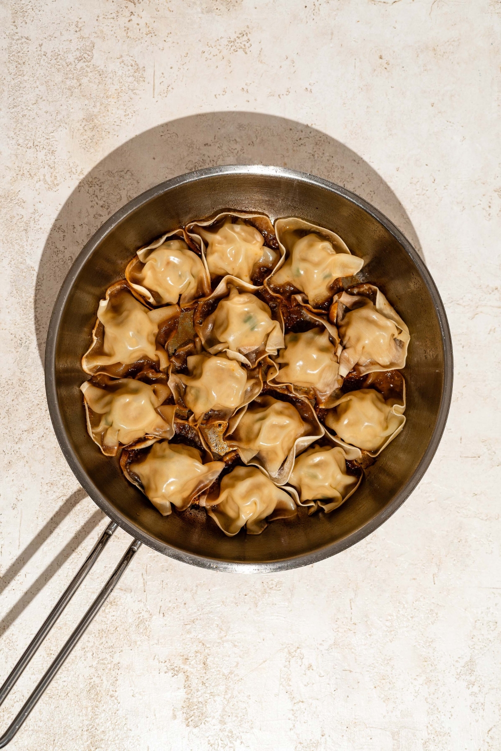 A skillet with steamed blanket dumplings. The skillet is on a tan counter.