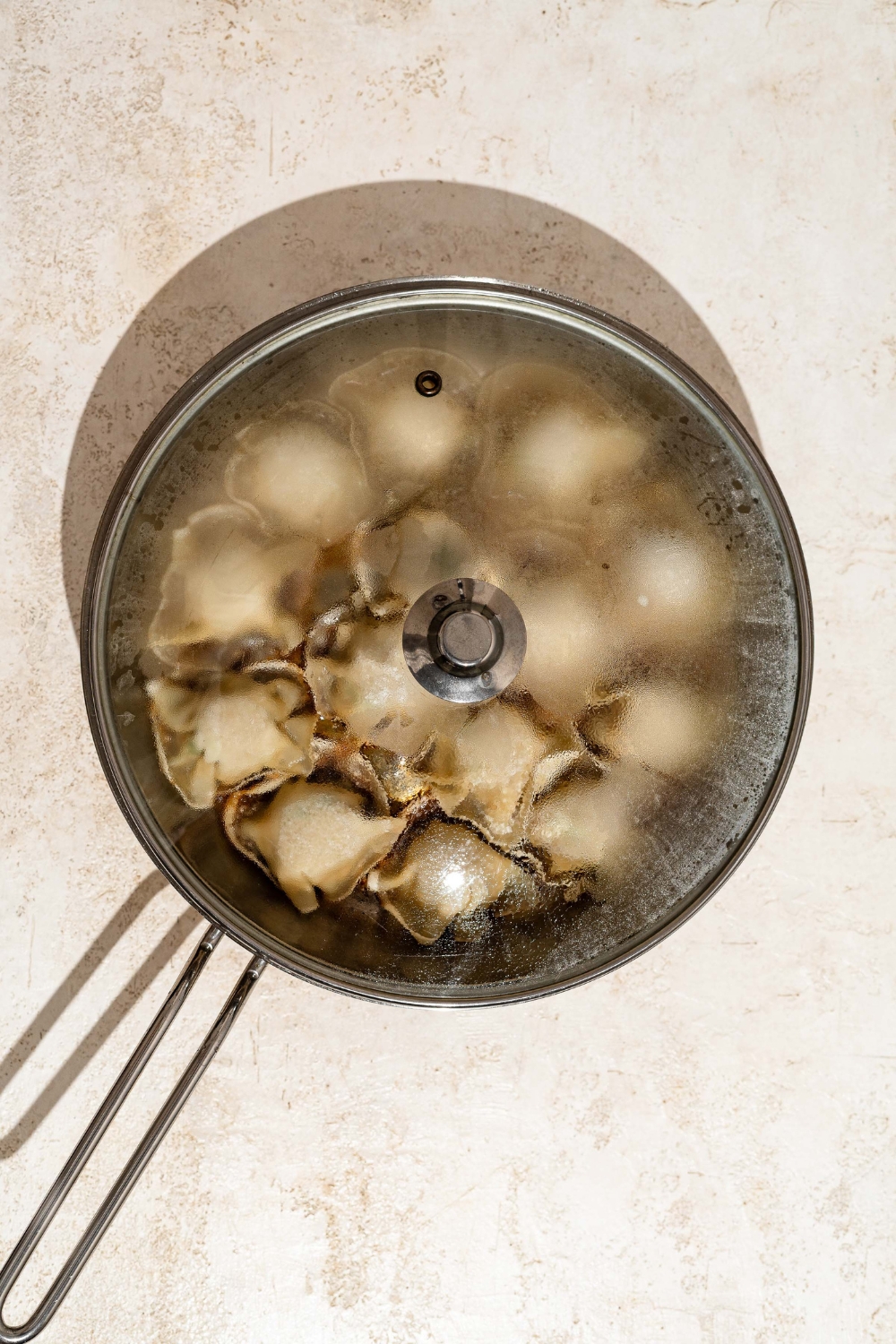 A covered skillet steaming blanket dumplings. The skillet is on a tan counter.