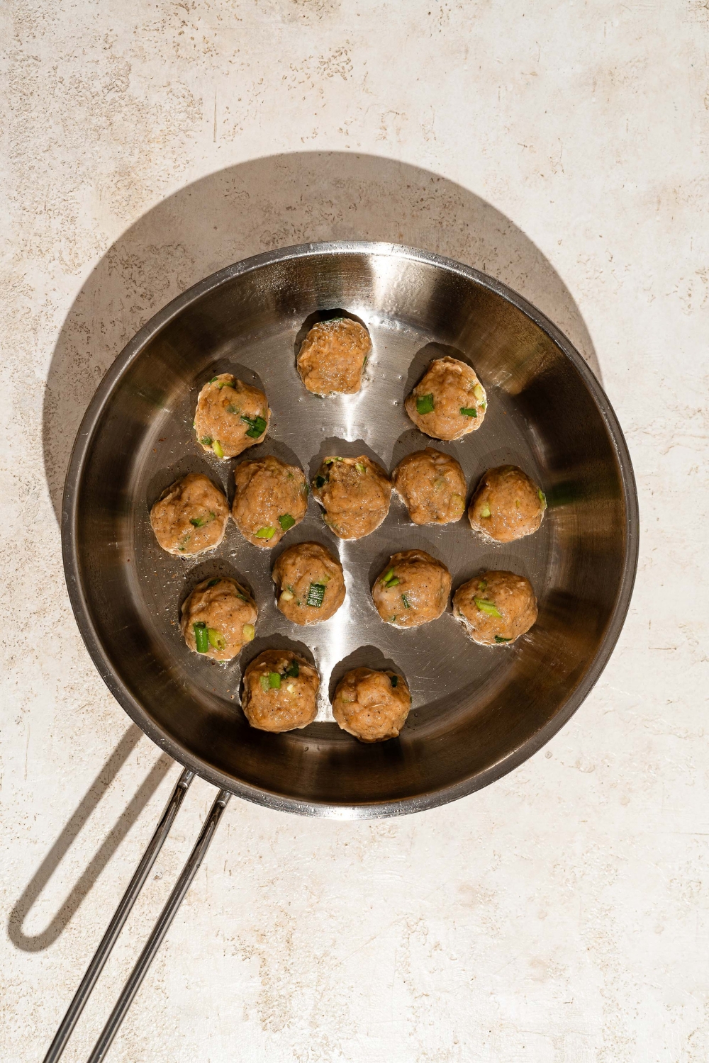 A skillet with several balls of ground pork mixture. The skillet is on a tan counter.