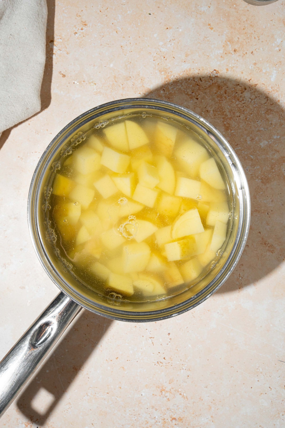 A pot with cubed potatoes boiling in water. The pot is on a tan counter.