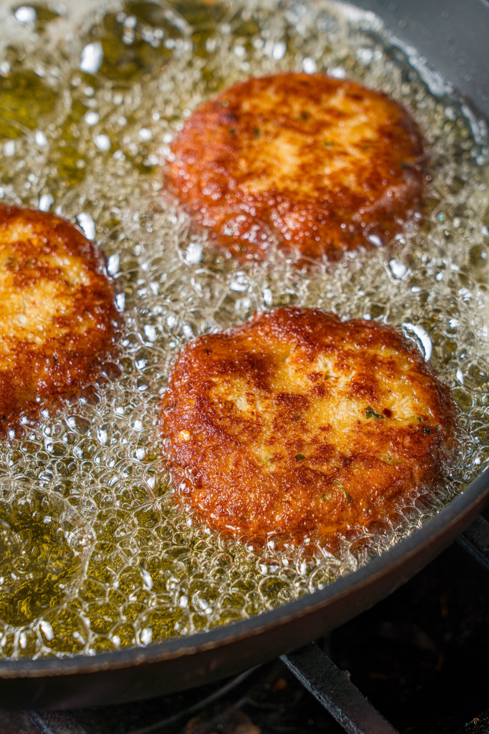 A frying pan with crab cakes frying in oil.