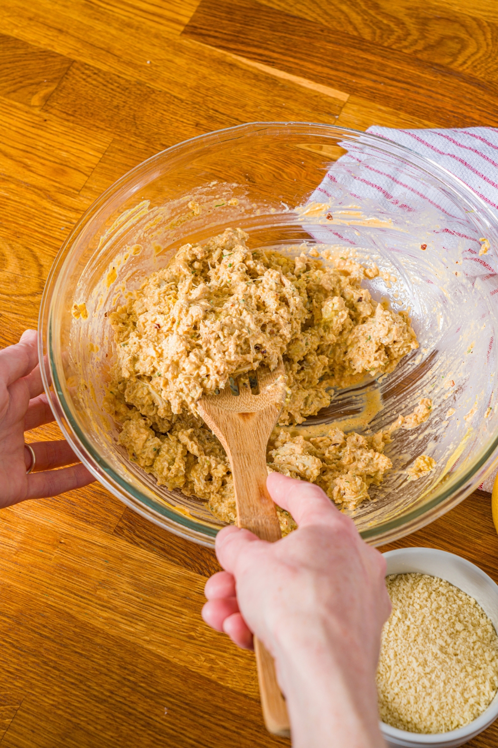 A large bowl with a wooden spoon mixing ingredients to make crab cakes. The bowl is on a wooden counter.