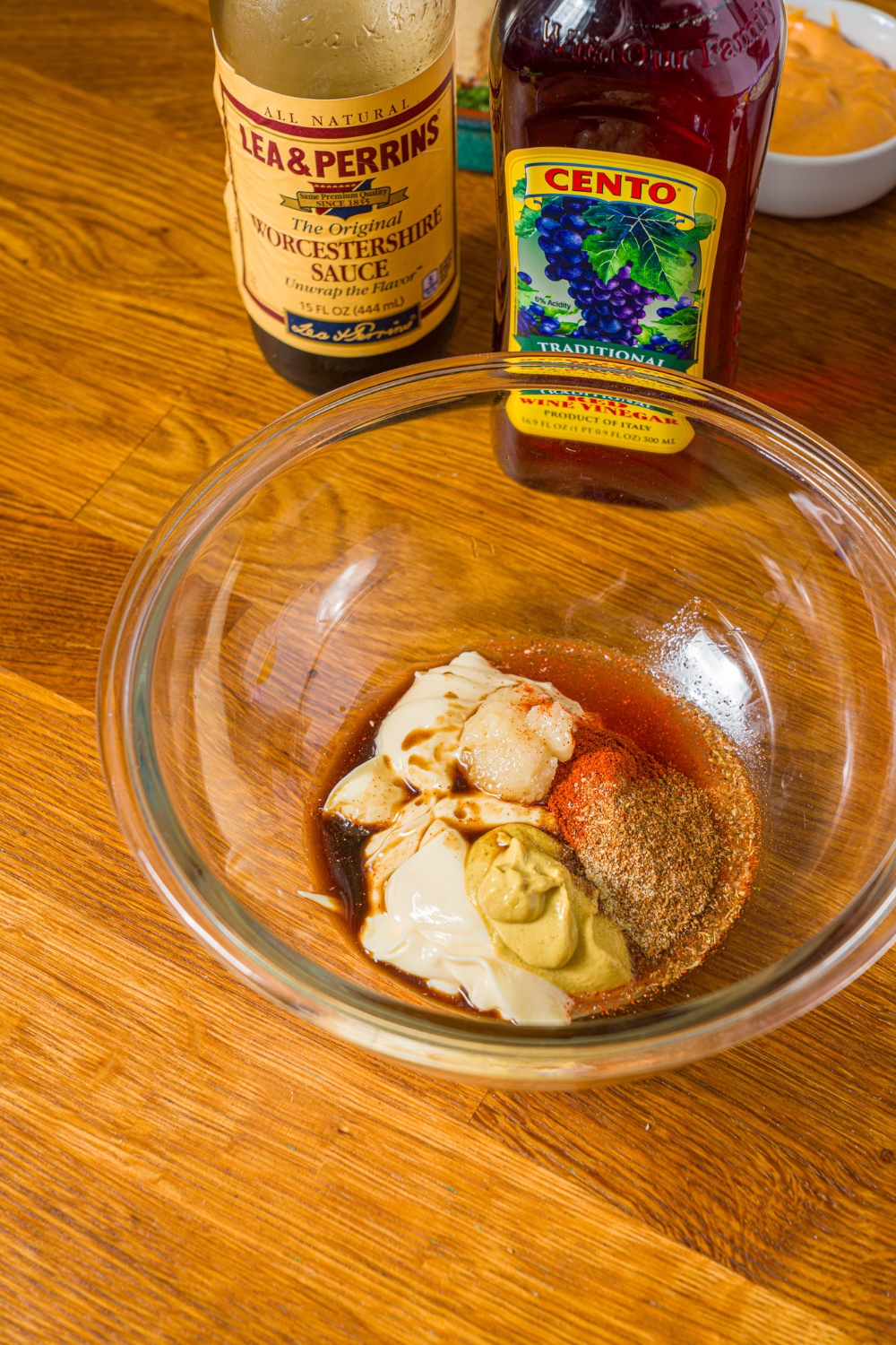 A bowl with ingredients to make crab cake sauce including mayonnaise, dijon mustard, red wine vinegar, Worcestershire sauce, and seasonings. The bowl is on a wooden counter.