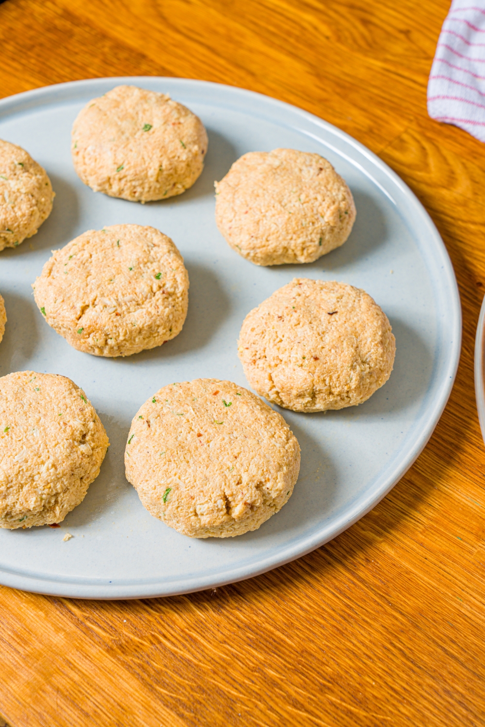 A plate with portioned uncooked crab cakes. The plate is on a wooden counter.