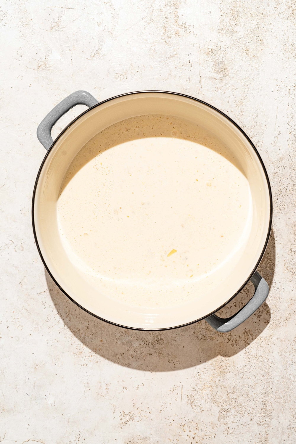 A large pot with ingredients to make alfredo sauce including sautéed garlic and heavy cream. The pot is on a tan counter.