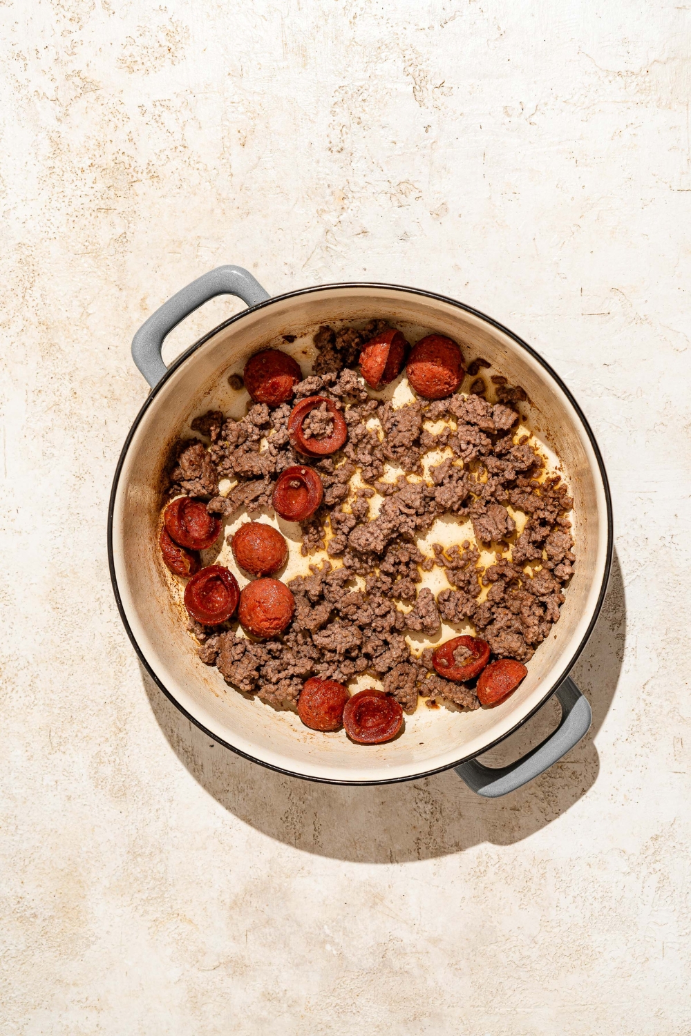 A dutch oven with sautéed sausage and ground beef. The dutch oven is on a tan counter.
