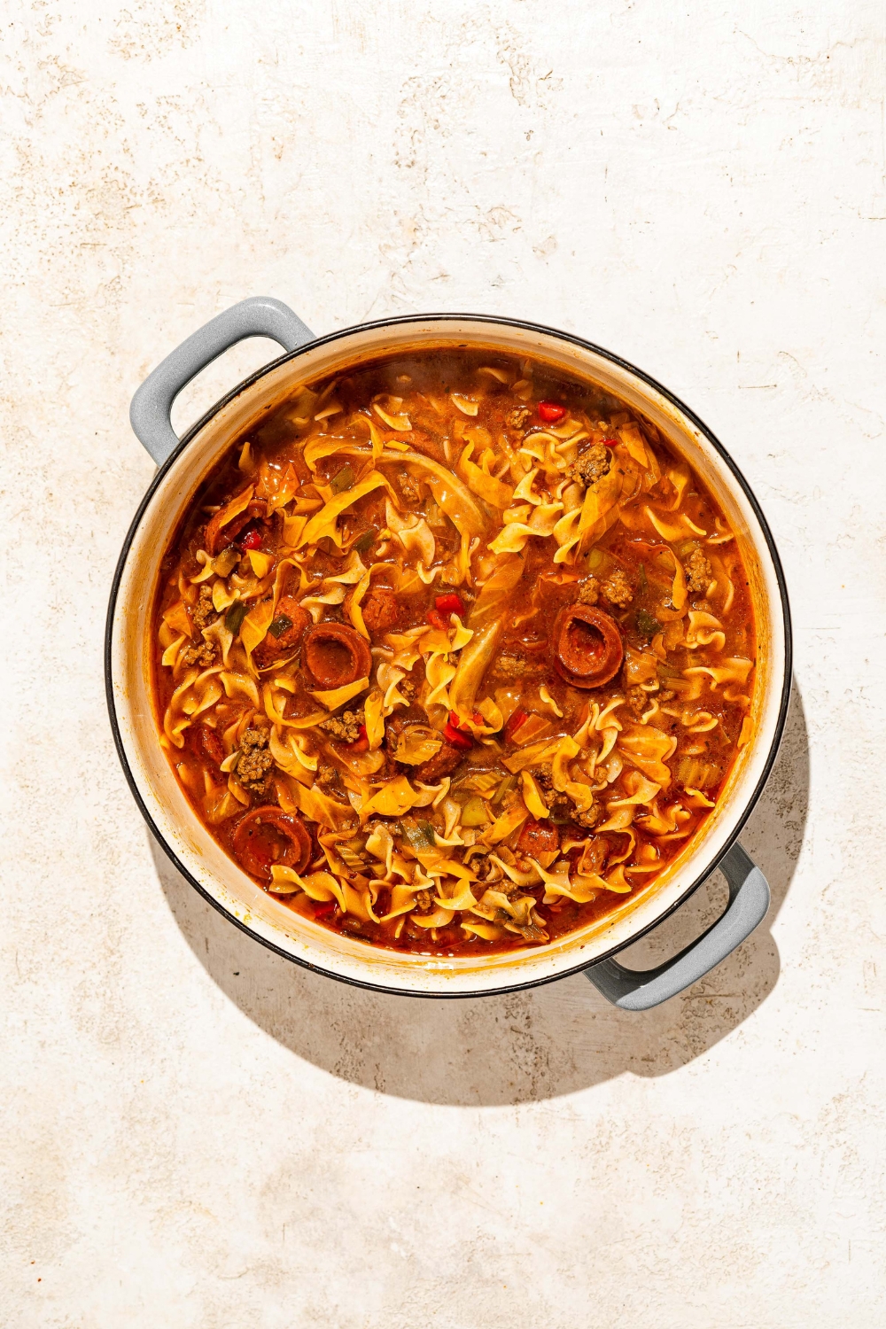 A dutch oven with cooked dirty cabbage tossed with noodles. The dutch oven is on a tan counter.
