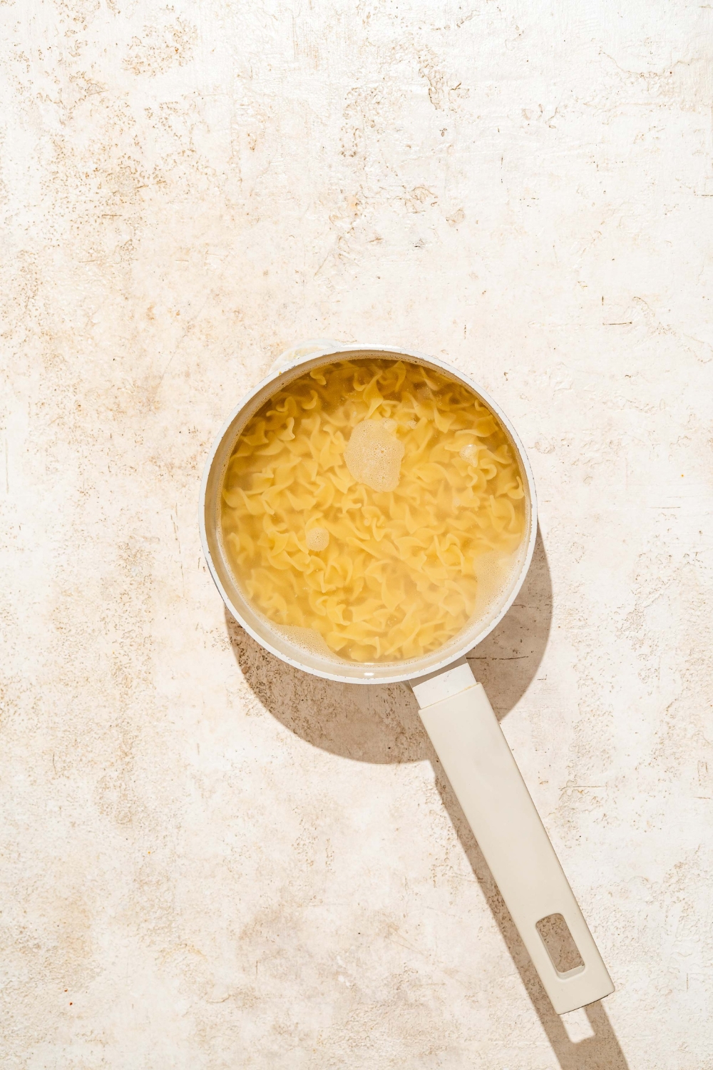 A pot with egg noodles cooking in water. The pot is on a tan counter.