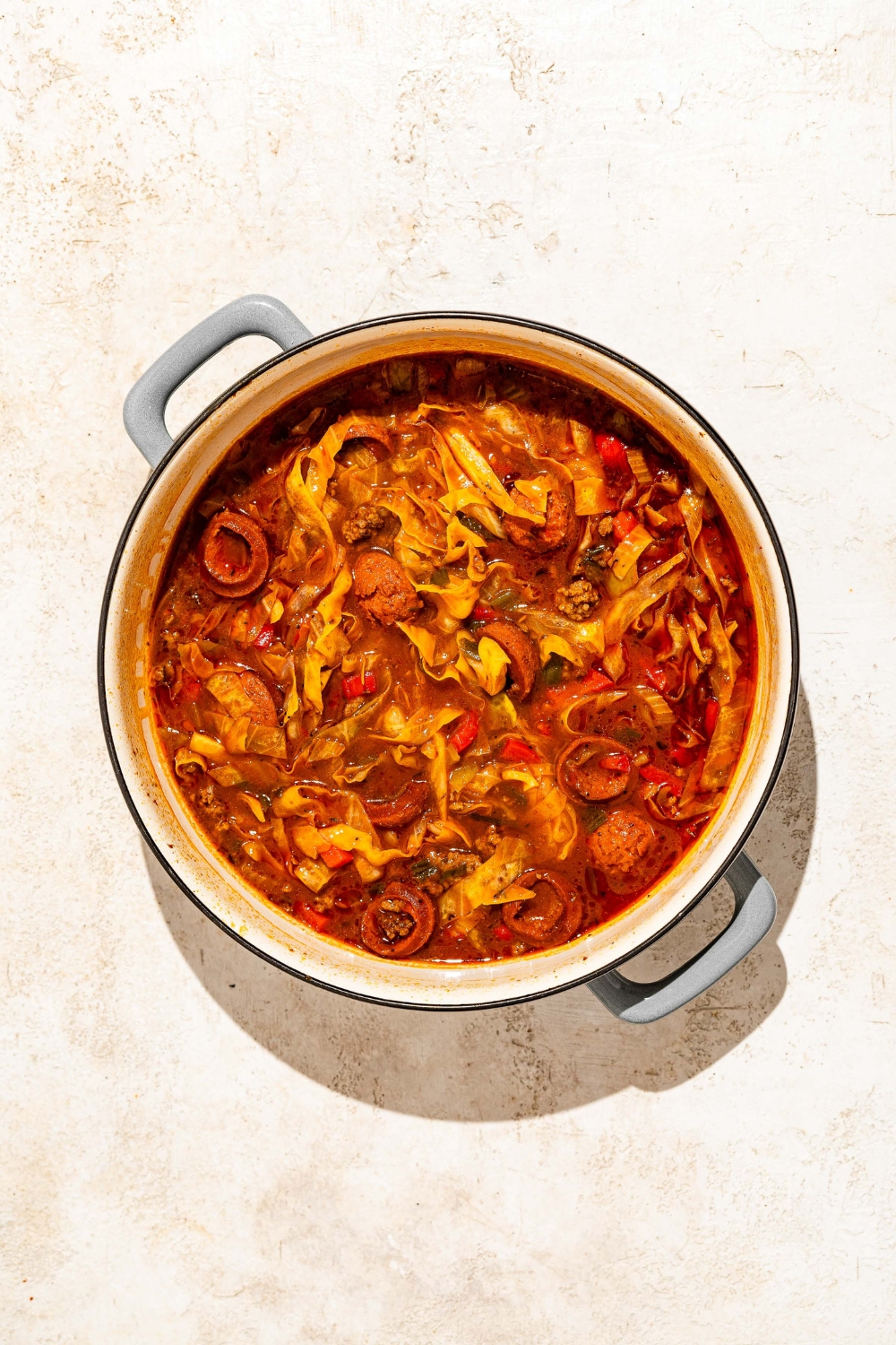 A dutch oven with dirty cabbage cooking in broth. The dutch oven is on a tan counter.