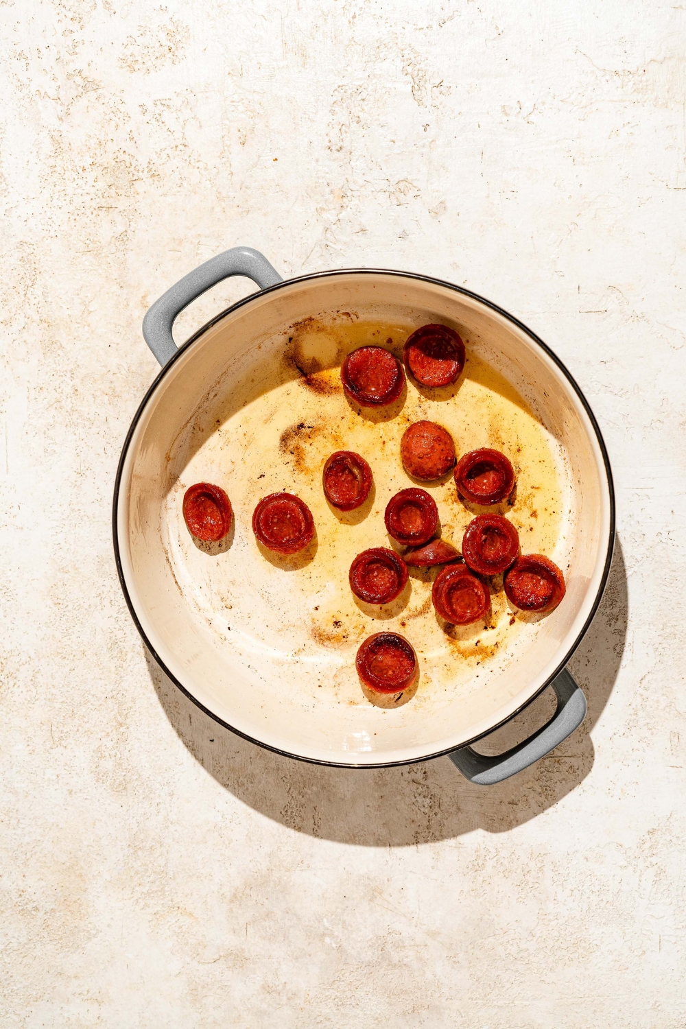 A dutch oven with browned andouille sausage. The dutch oven is on a tan counter.