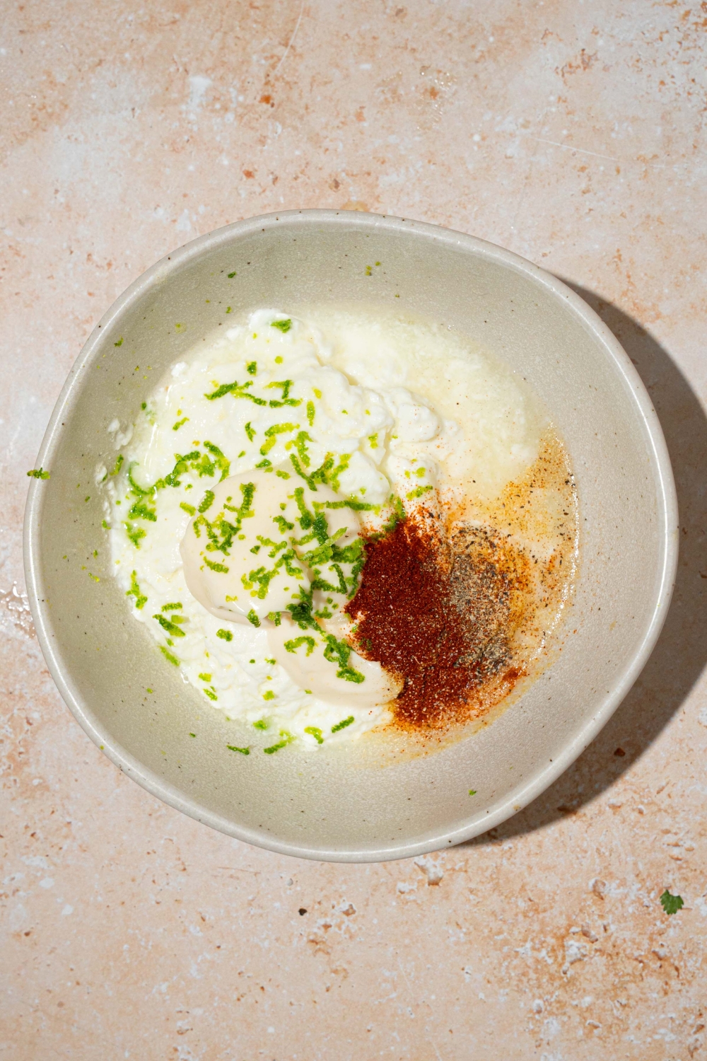 A white bowl with greek yogurt, mayo, lime juice, and seasonings. The bowl is on a tan counter.