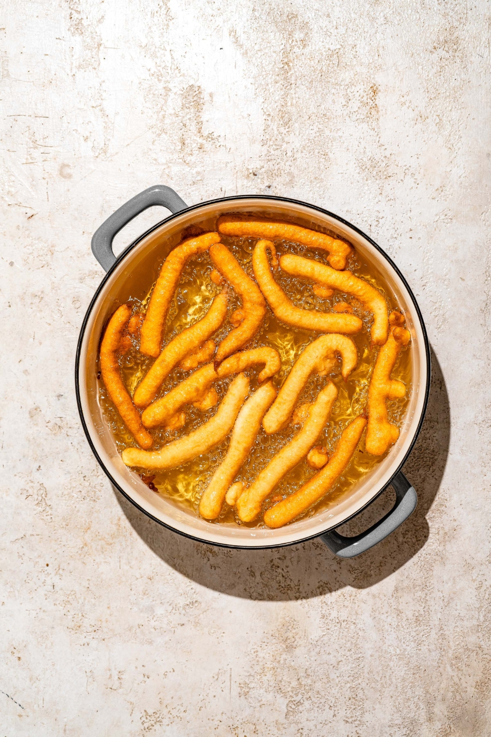 A large pot with funnel cake fries cooking in hot oil. The pot is on a tan counter.