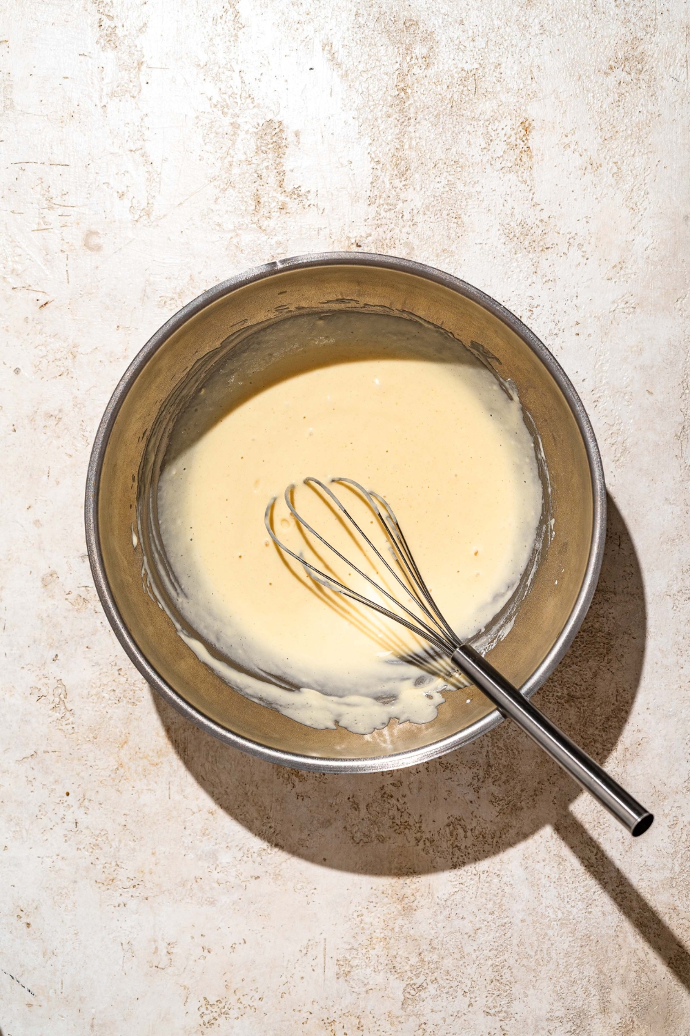 A large bowl with a whisk mixing funnel cake batter. The bowl is on a tan counter.