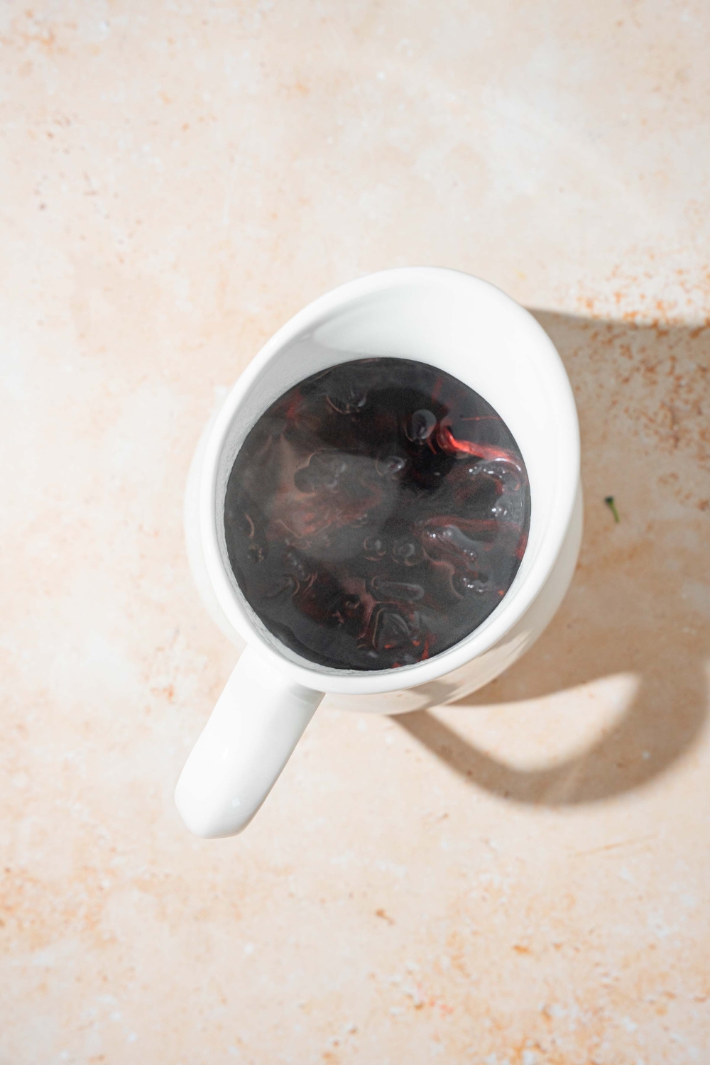 A tea pitcher with hot hibiscus tea. The pitcher is on a tan counter.