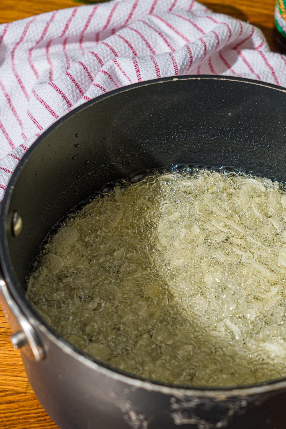 A large pot with sliced garlic cooking in oil. The pot is on a wooden counter with a white striped napkin.