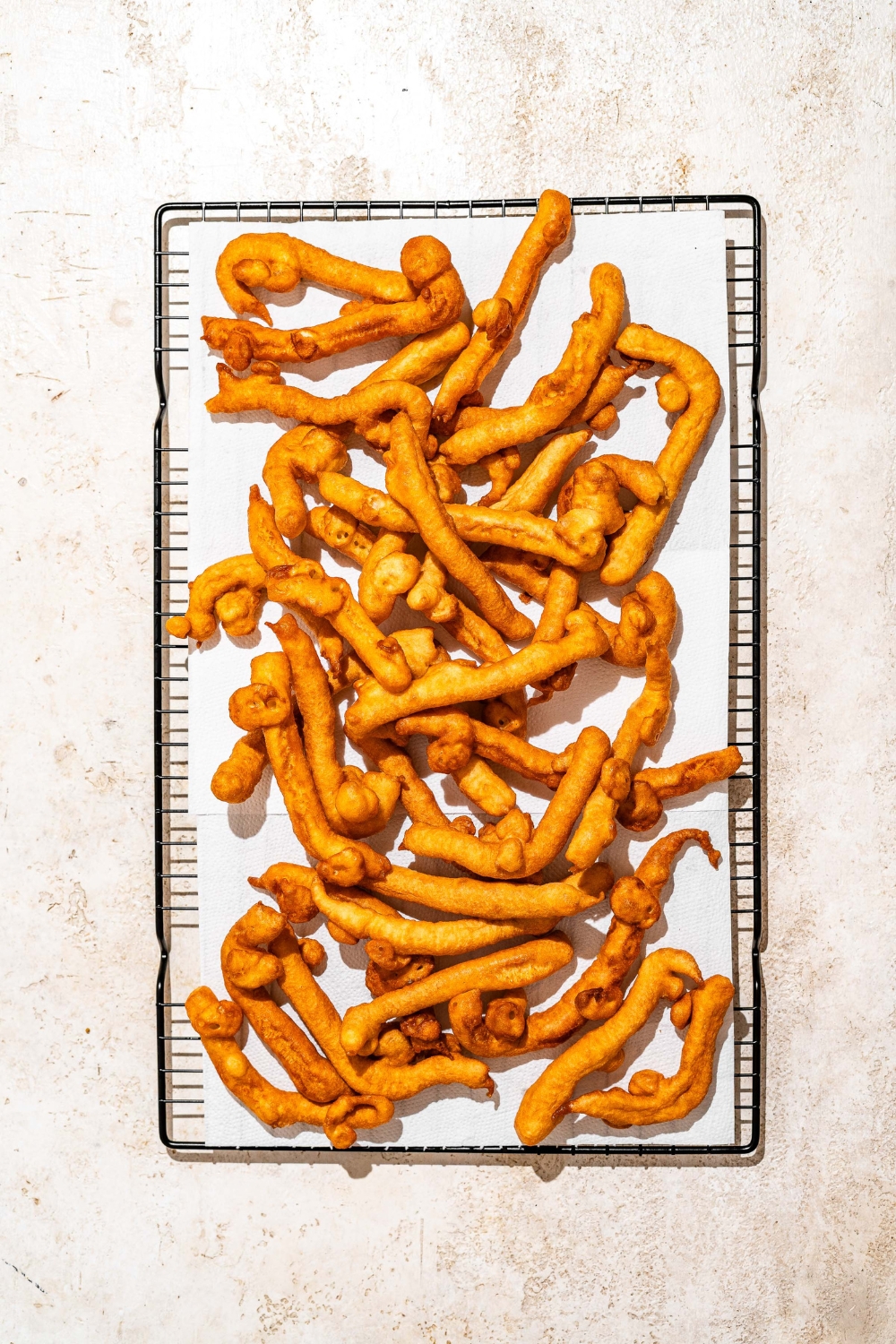 A wire rack lined with parchment paper with fried funnel cake fries. The rack is on a tan counter.