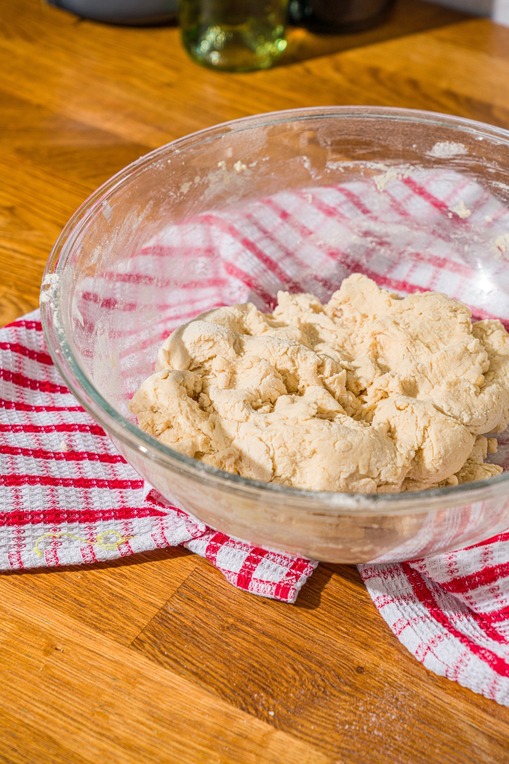 A glass bowl with homemade hoagie rolls dough mixture. The bowl is on a wooden counter with a red striped napkin.