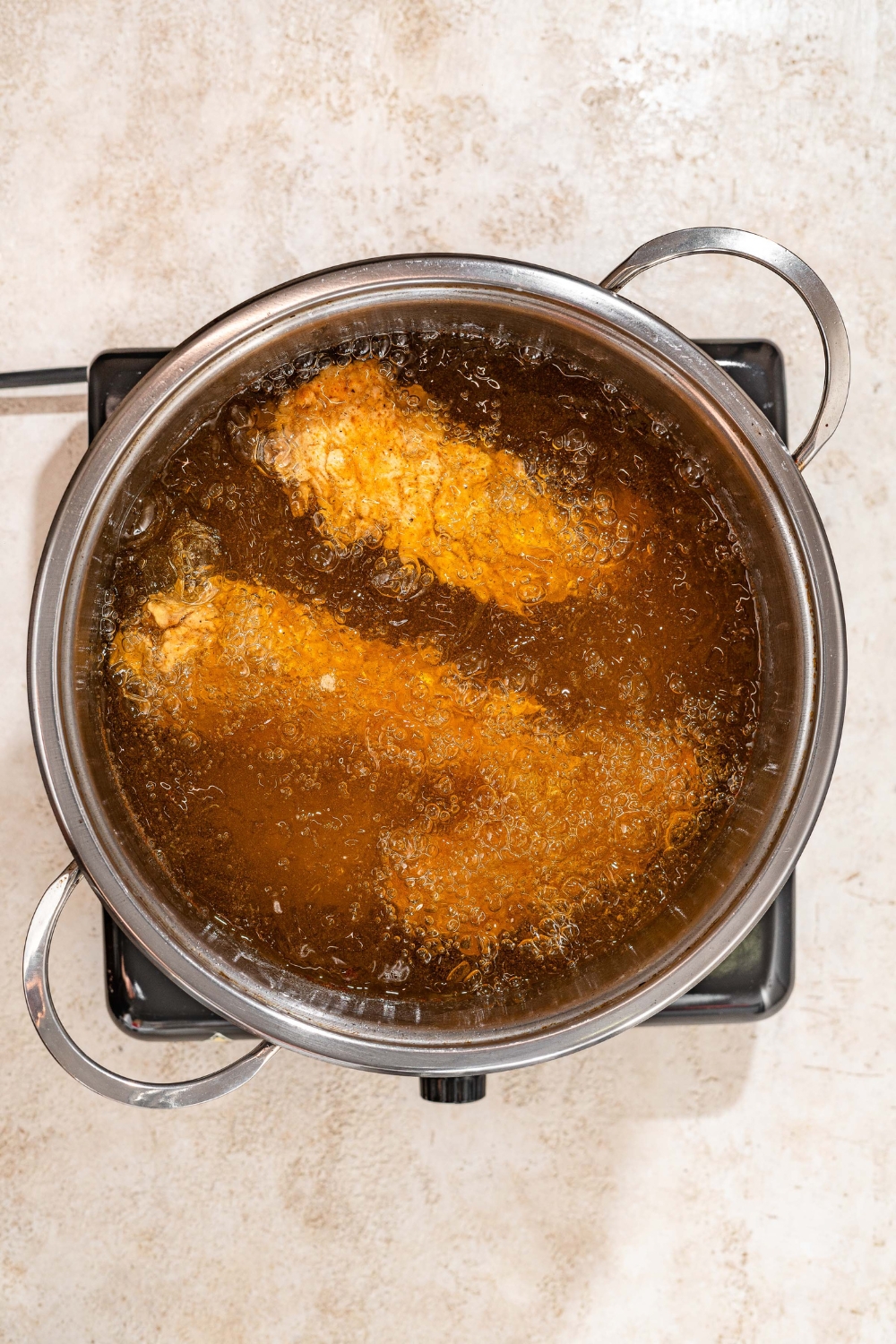 A pot of breaded chicken tenders frying in oil. The pot is on a tan counter.