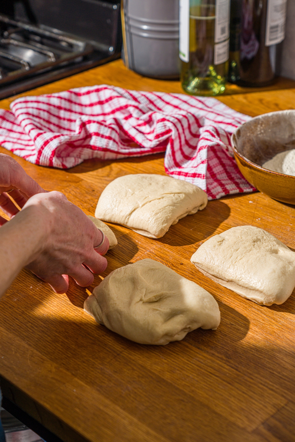 Hoagie roll dough being sliced into quarters on a wooden counter with a red striped napkin.
