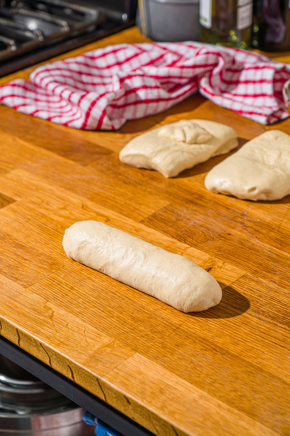 Hoagie roll dough shaped into a roll on a wooden counter with additional pieces of dough.