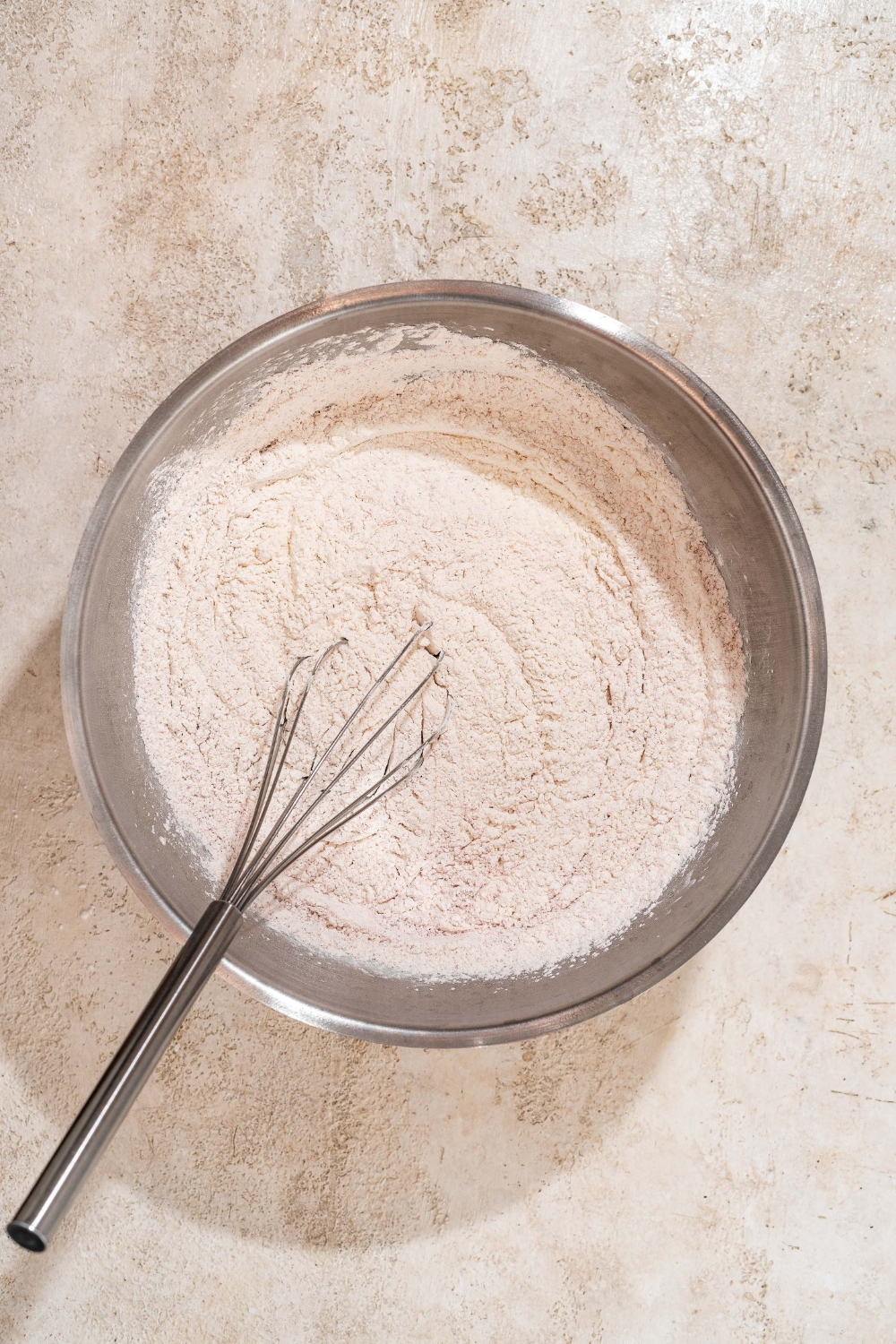 A large bowl with a whisk mixing ingredients for a dry marinade mixture. The bowl is on a tan counter.
