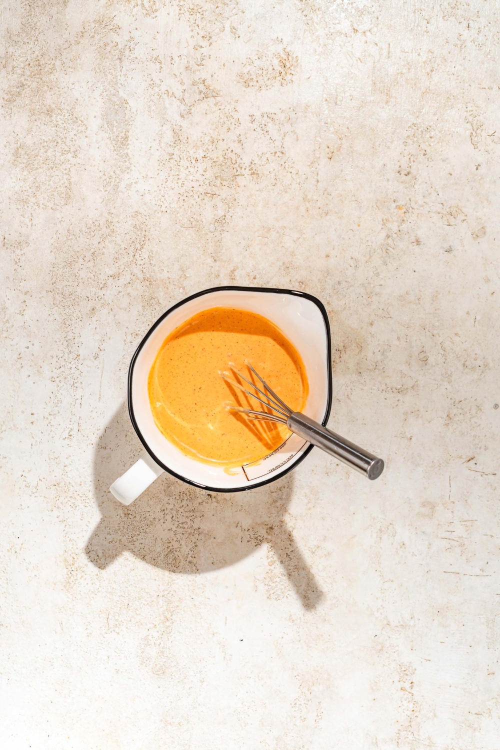 A bowl with a whisk mixing a chipotle mayo. The bowl is on a tan counter.