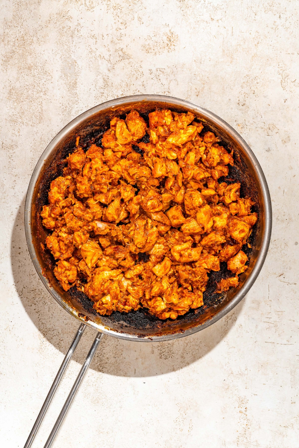A skillet with cooked marinated chicken. The skillet is on a tan counter.