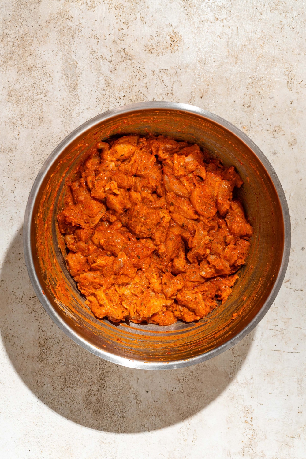 A large bowl with cubed chicken marinating in marinade. The bowl is on a tan counter.