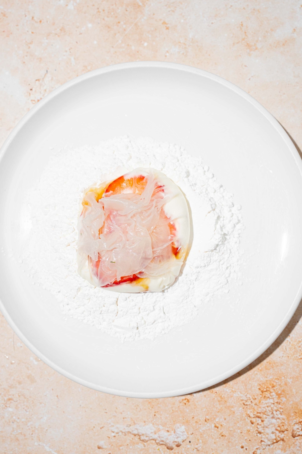 A white plate with a rice paper mochi wrapped with honey and strawberry. The rice paper ball is on a pile of rice flour.