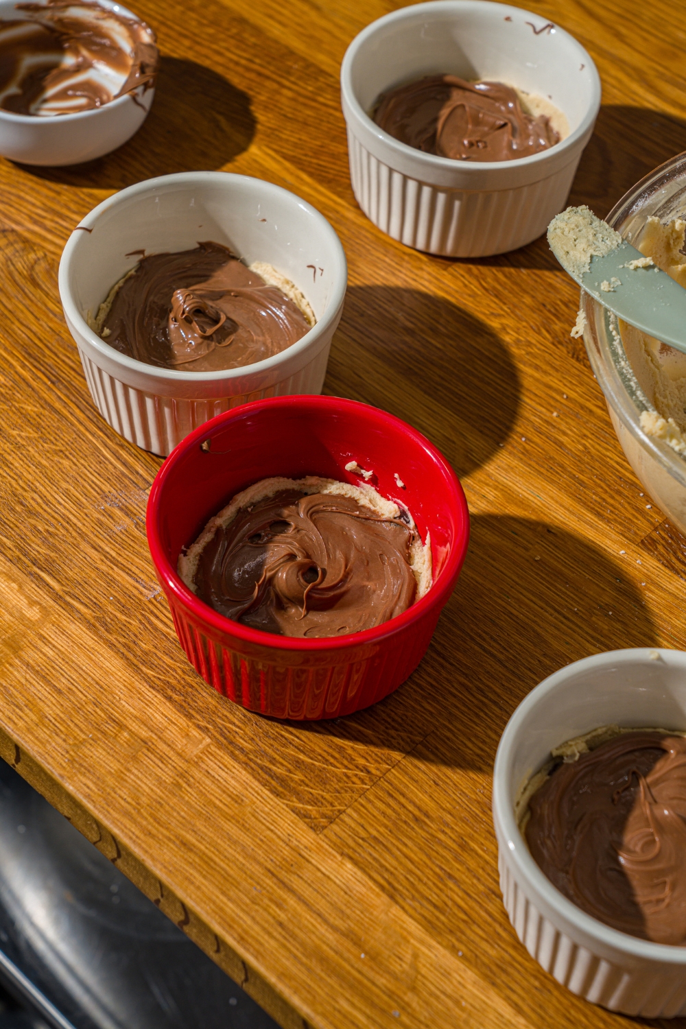 Several ramekins with raw cookie dough layered with nutella. The ramekins are on a wooden counter.