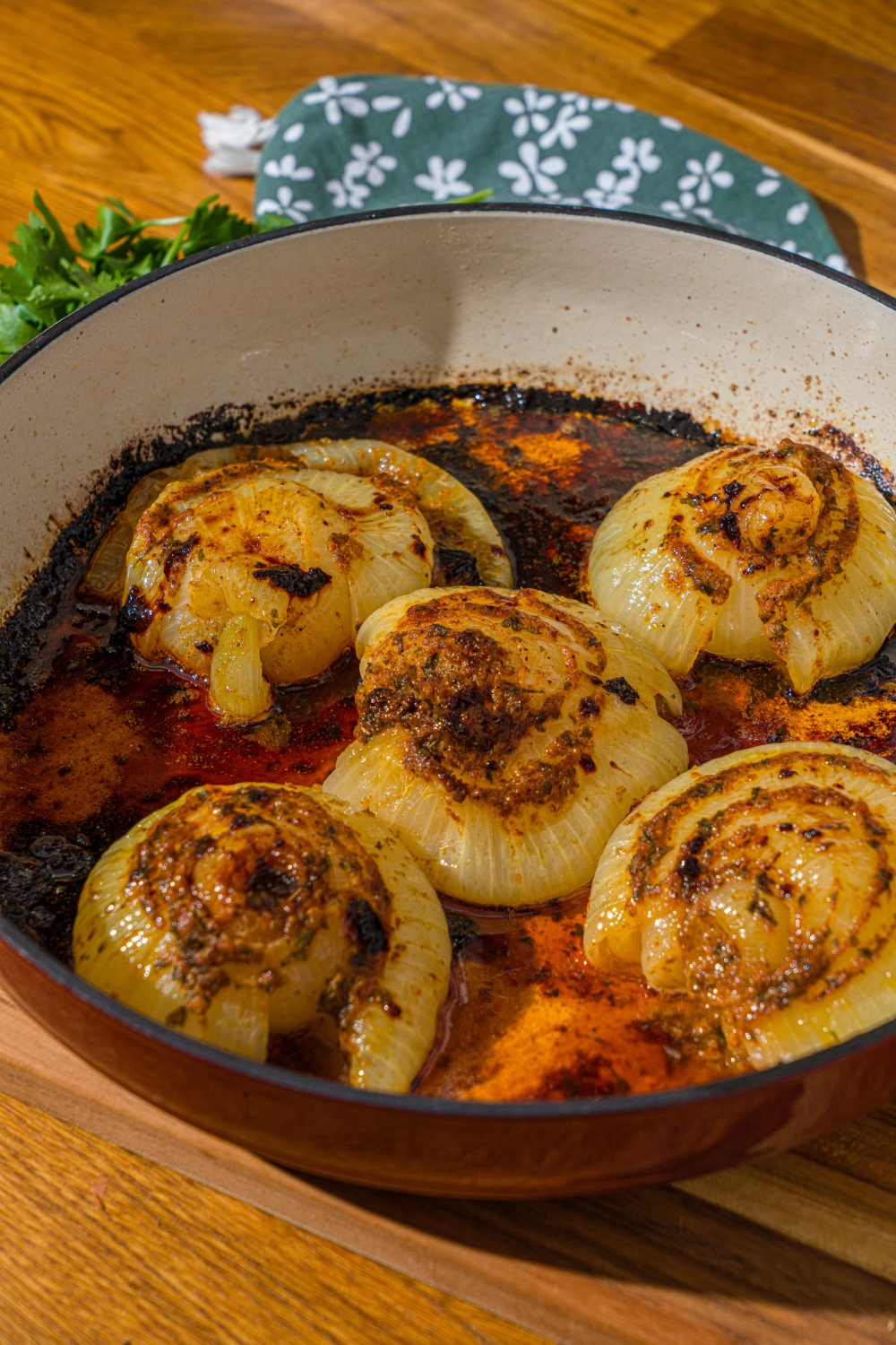 A dutch oven with cook onion boil with seasoned butter sauce. The dutch oven is on a wooden counter with a green floral napkin.