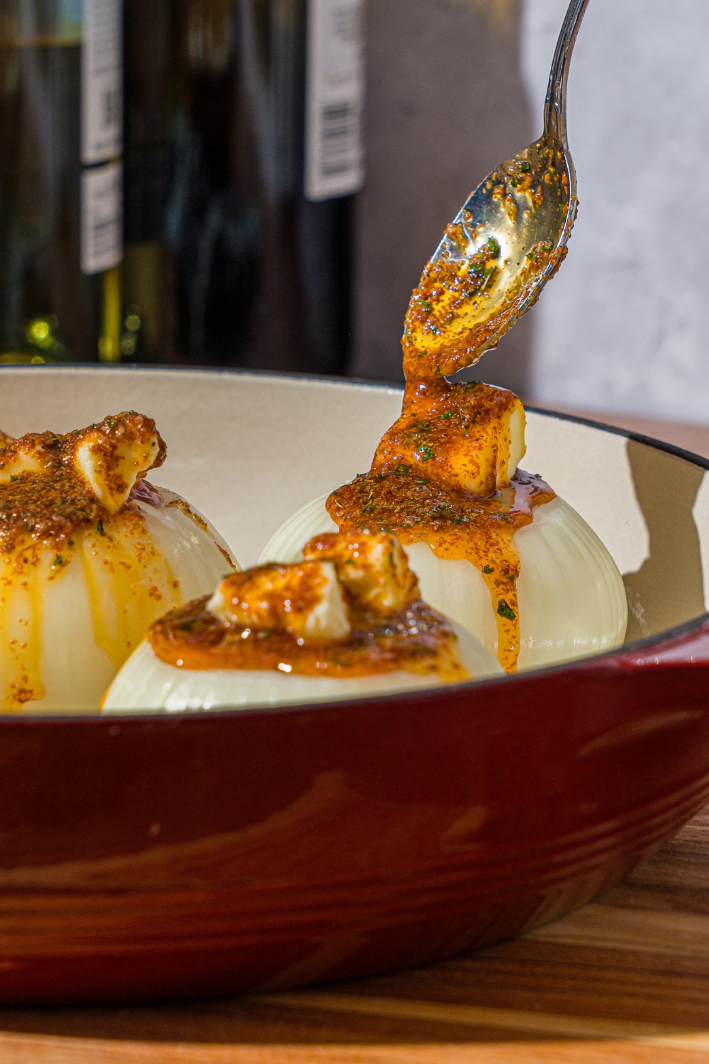 A dutch oven with a spoon pouring seasoned butter sauce over onions stuffed with butter.
