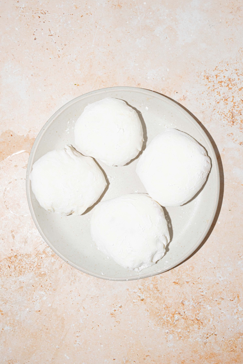 A plate with four rice paper mochi balls rolled in rice flour. The plate is on a tan counter.