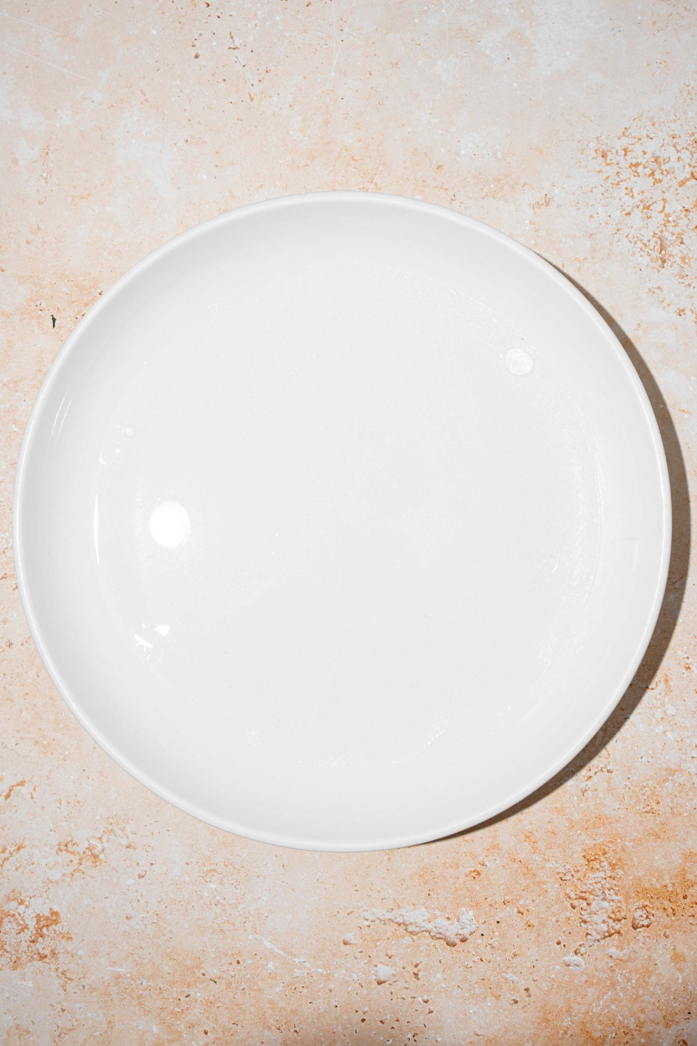 A white bowl with rice paper soaking in water. The bowl is on a tan counter.