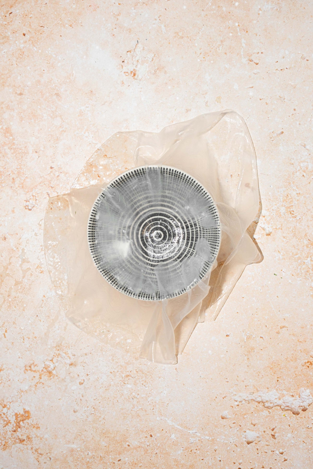 A cup with a soaked rice paper sheet formed in the cup. The cup is on a tan counter.