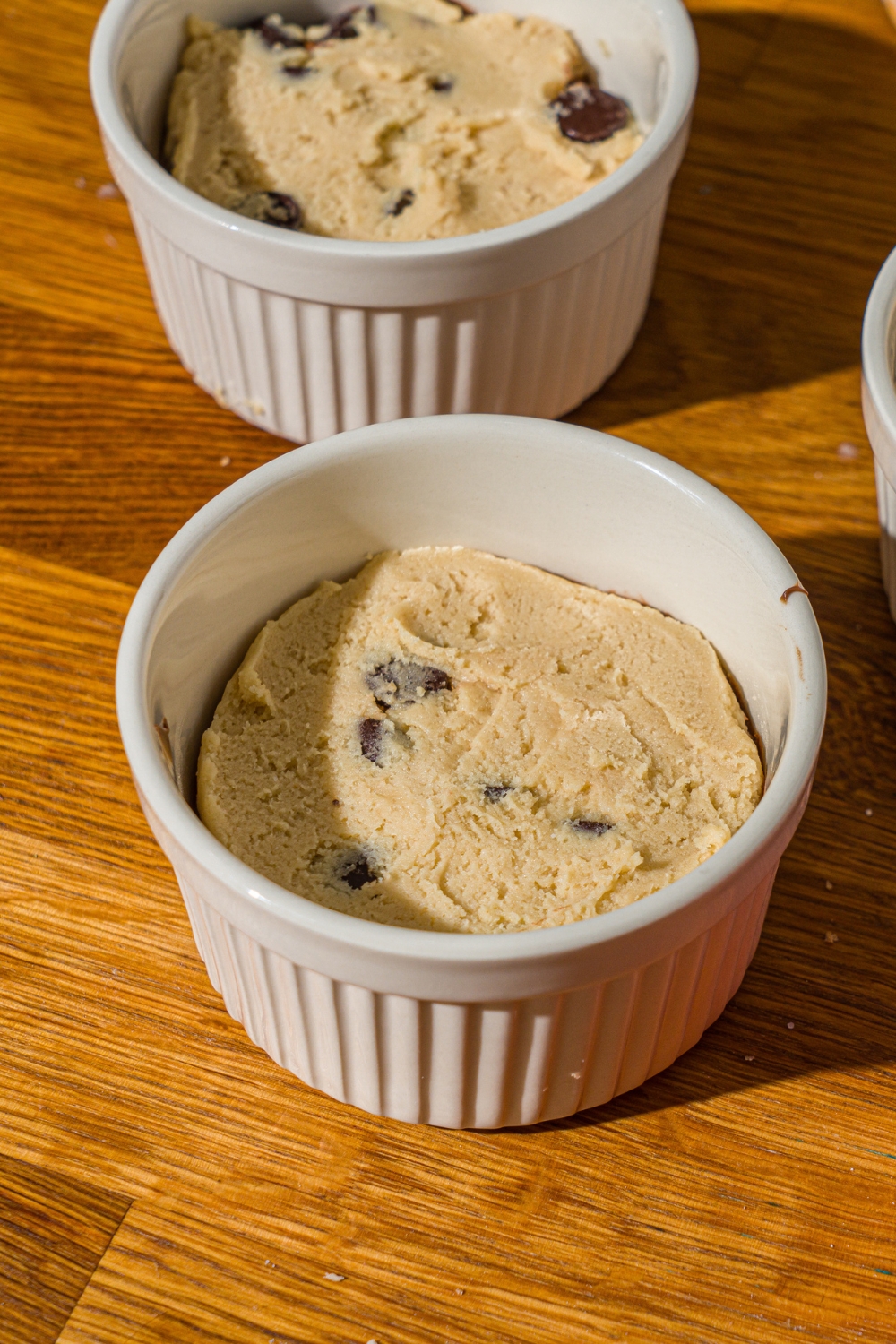 A ramekin with raw cookie dough layered with nutella. The ramekins are on a wooden counter.