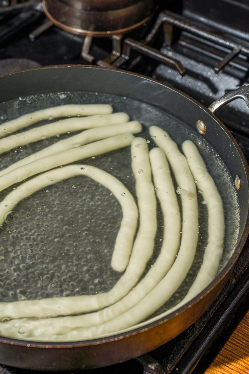 A pot of boiling water with potato noodles cooking on the stove.