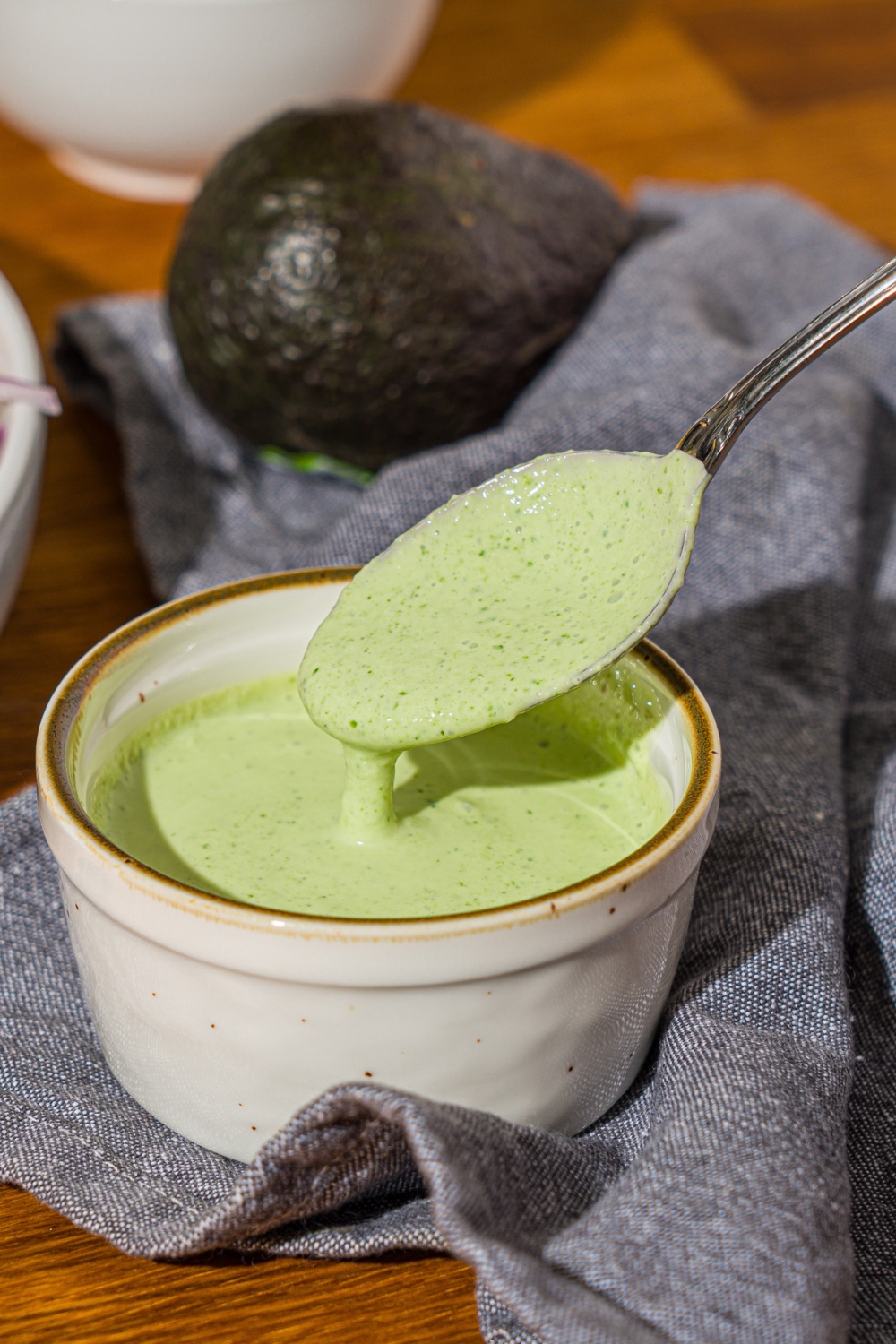 A small ramekin of cilantro lime sauce with a spoon dipping in the bowl. The bowl is on a wooden counter with a blue cloth napkin.