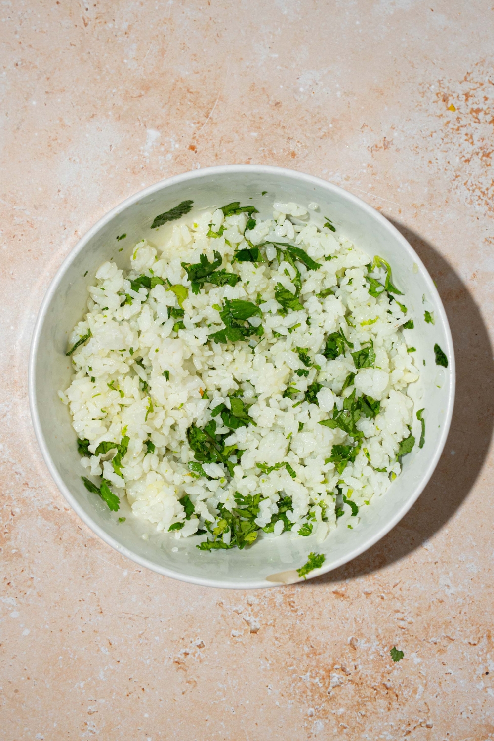A large white bowl with cilantro lime rice. The bowl is on a tan counter.