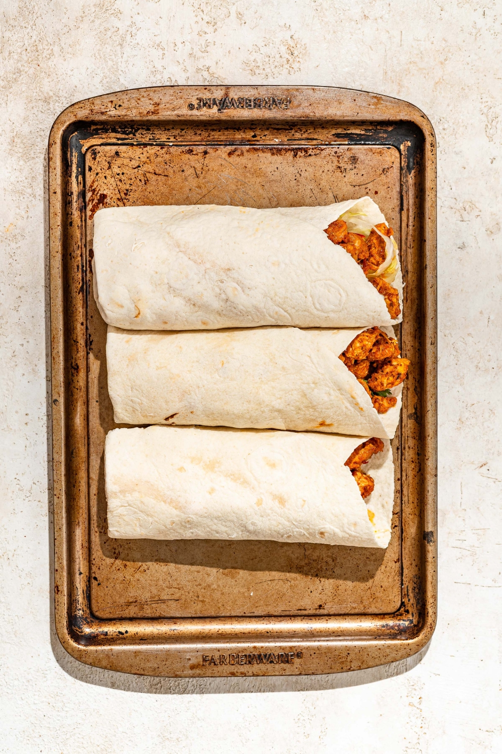 A baking sheet with three honey chipotle chicken wraps. The sheet is on a tan counter.