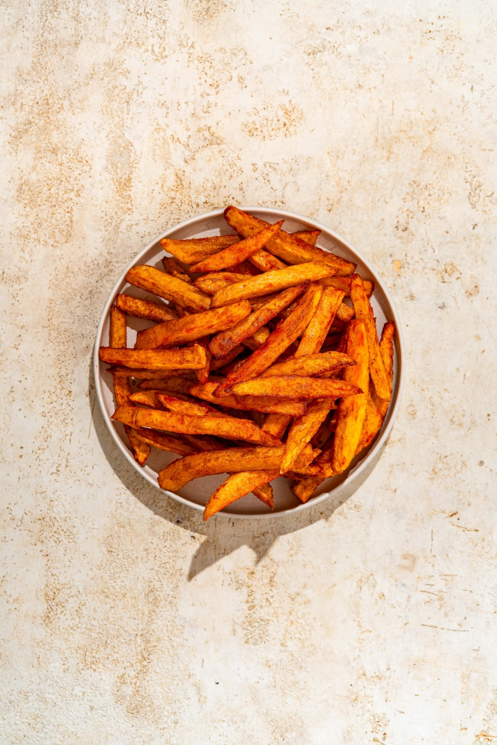 A white plate with crispy seasoned fries. The plate is on a tan counter.