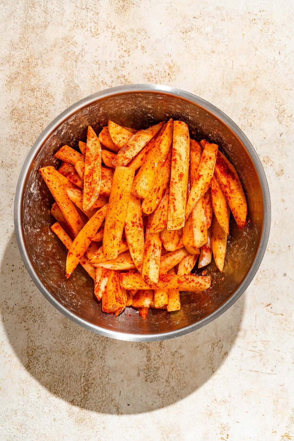 A large bowl with cut fries tossed in seasonings. The bowl is on a tan counter.