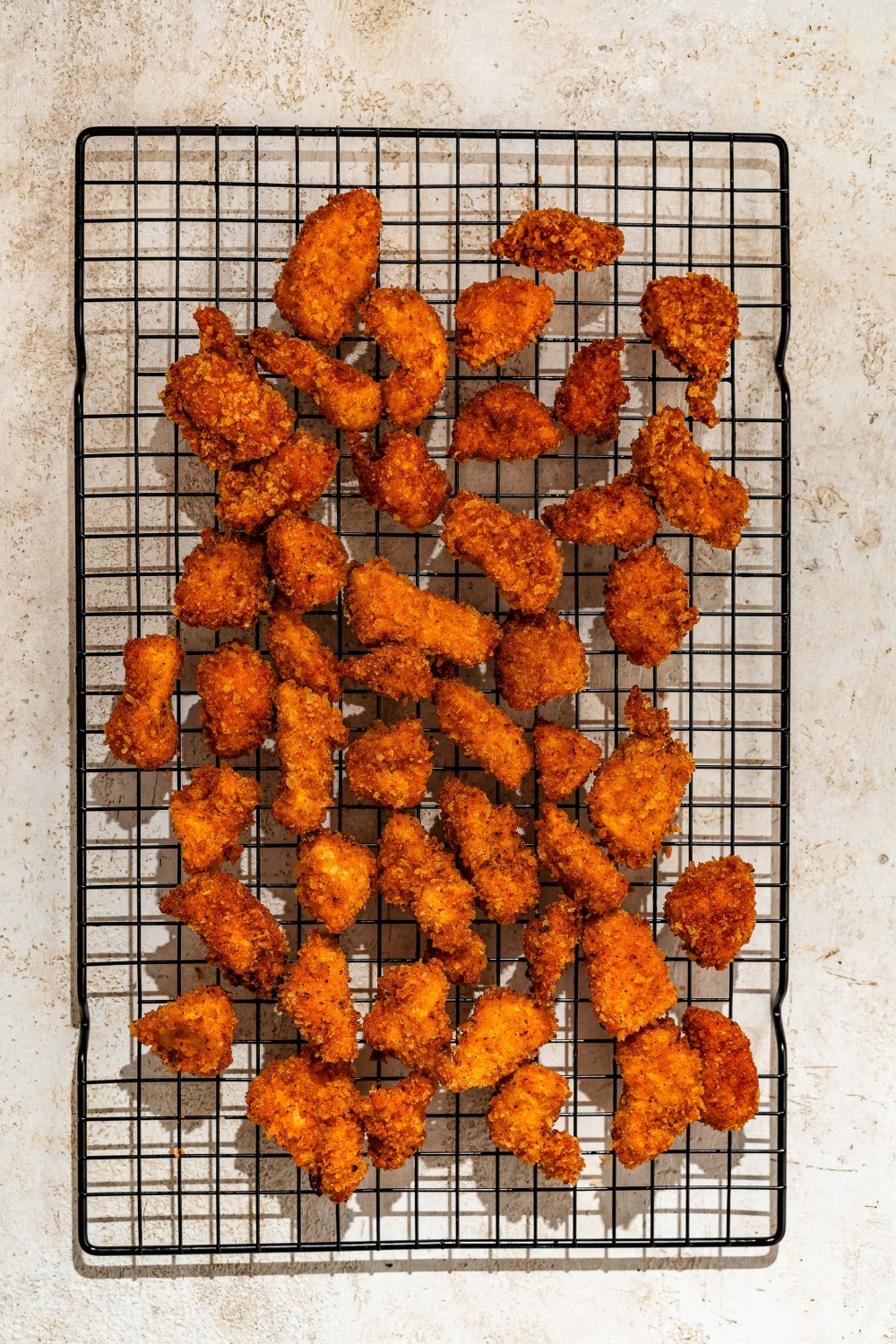 A wire rack with crispy chicken bites. The rack is on a tan counter.