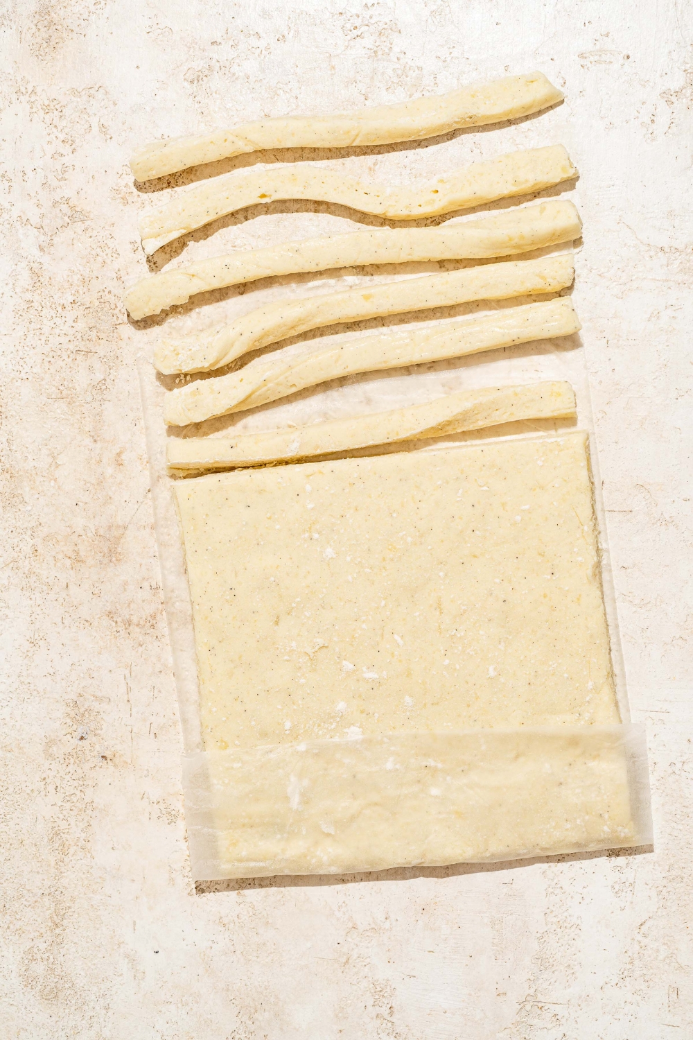 A tan counter with chilled and rolled Japanese long fry dough with several fries sliced from the dough.