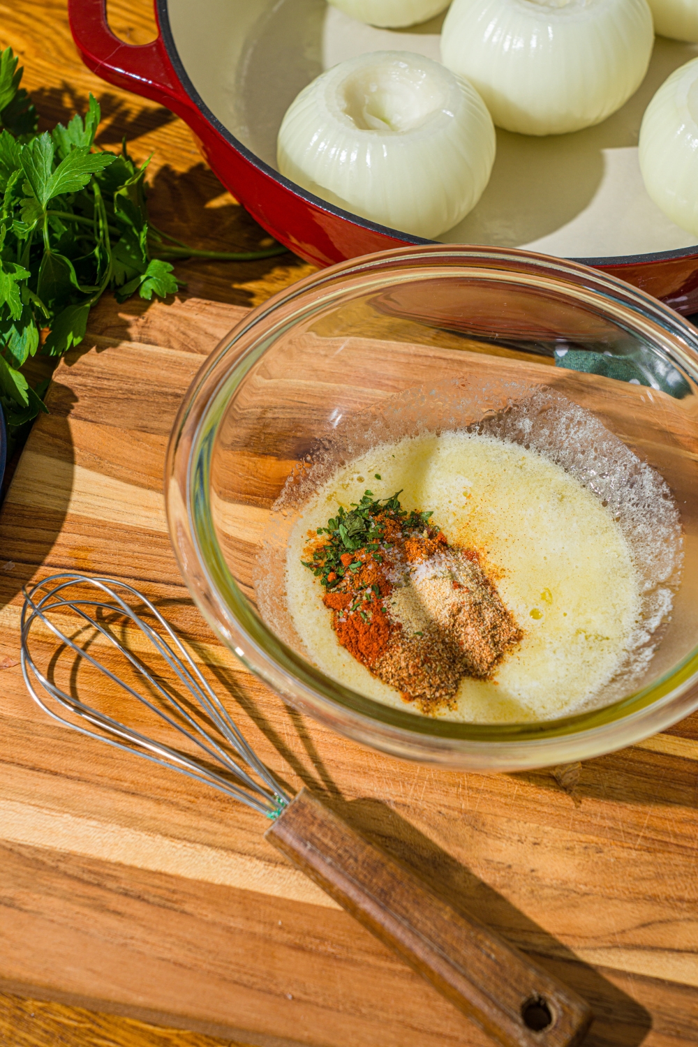 A glass bowl with melted butter and seasonings. The bowl is on a wooden counter with a whisk.